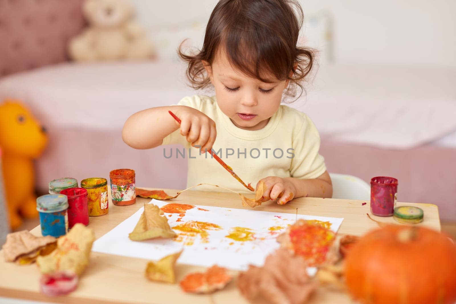 cute little child girl painting autumn leaves. baby girl drawing leaves in yellow and orange paint