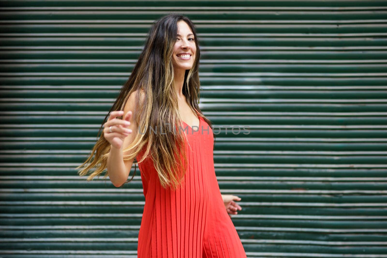 A lively young woman with long braided hair dances joyfully in a vibrant red dress, contrasting with a lush green backdrop, exuding an aura of energy and positivity that is contagious