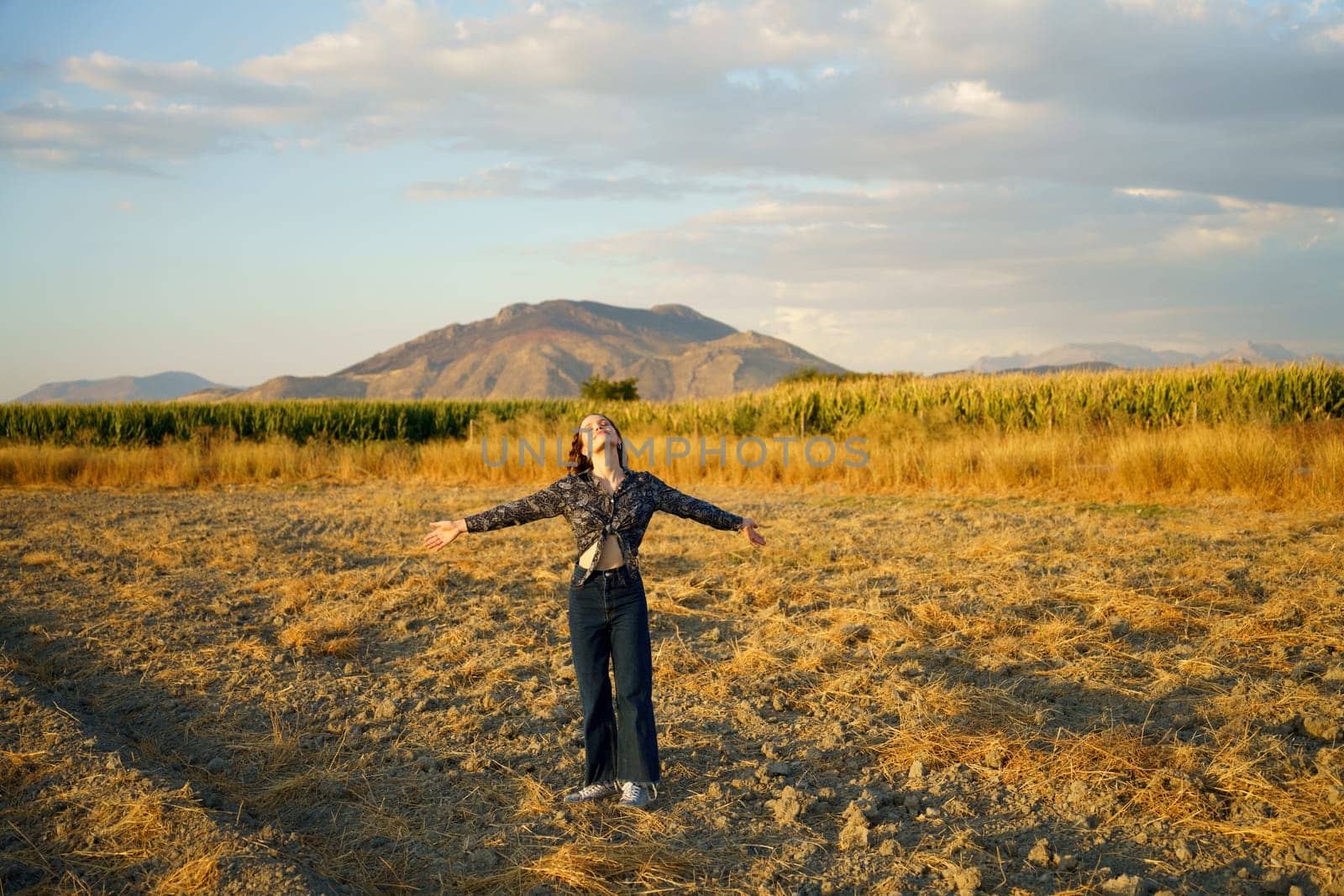 A person joyfully embraces freedom in a stunning golden field under a beautifully painted sky, with rolling hills as an idyllic backdrop, capturing the essence of nature and pure joy