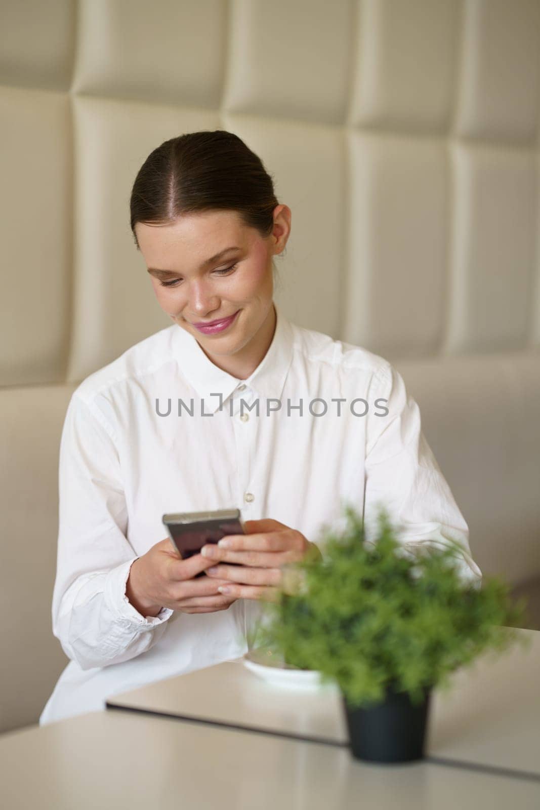 Vertical portrait of a smiling concentrated woman using phone in a modern cafeteria