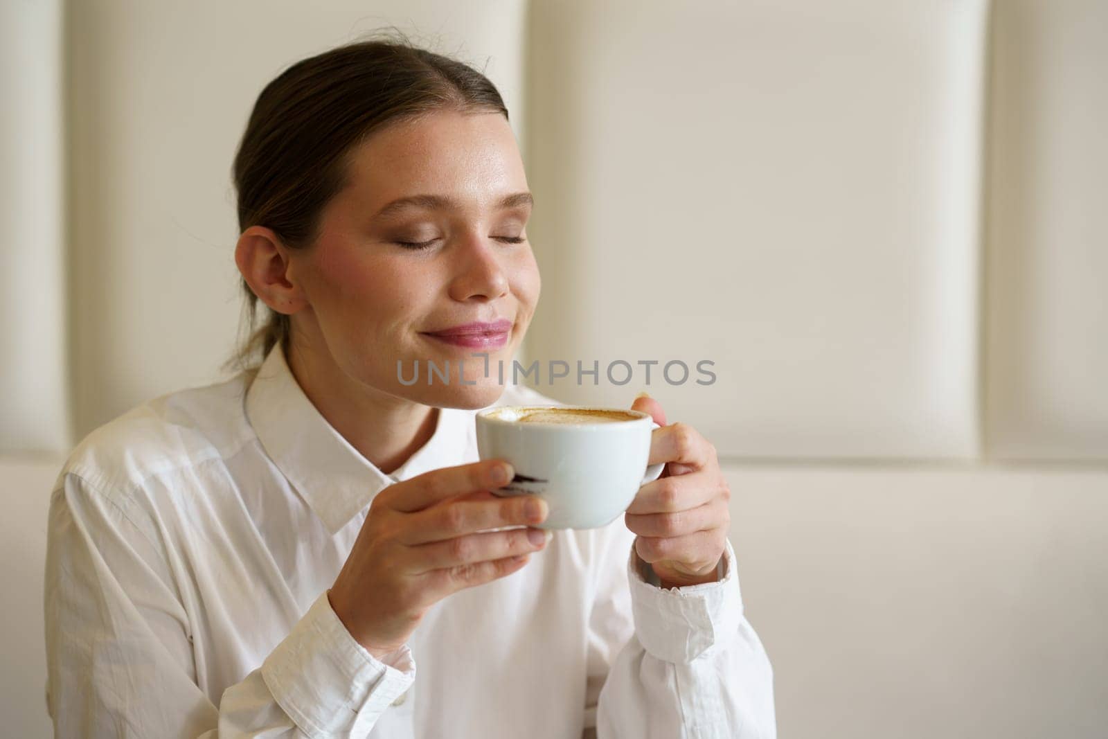 Beauty woman closing the eyes to enjoy the aroma and taste of a latte coffee in a modern cafeteria