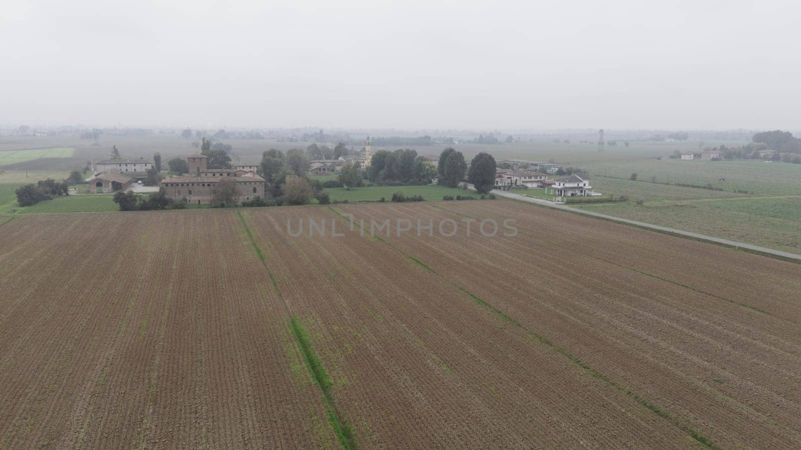 Piacenza, Italy October 15th 2024 An aerial view of cultivated fields and farmhouses in the italian countryside on a foggy day with the sky completely covered by clouds