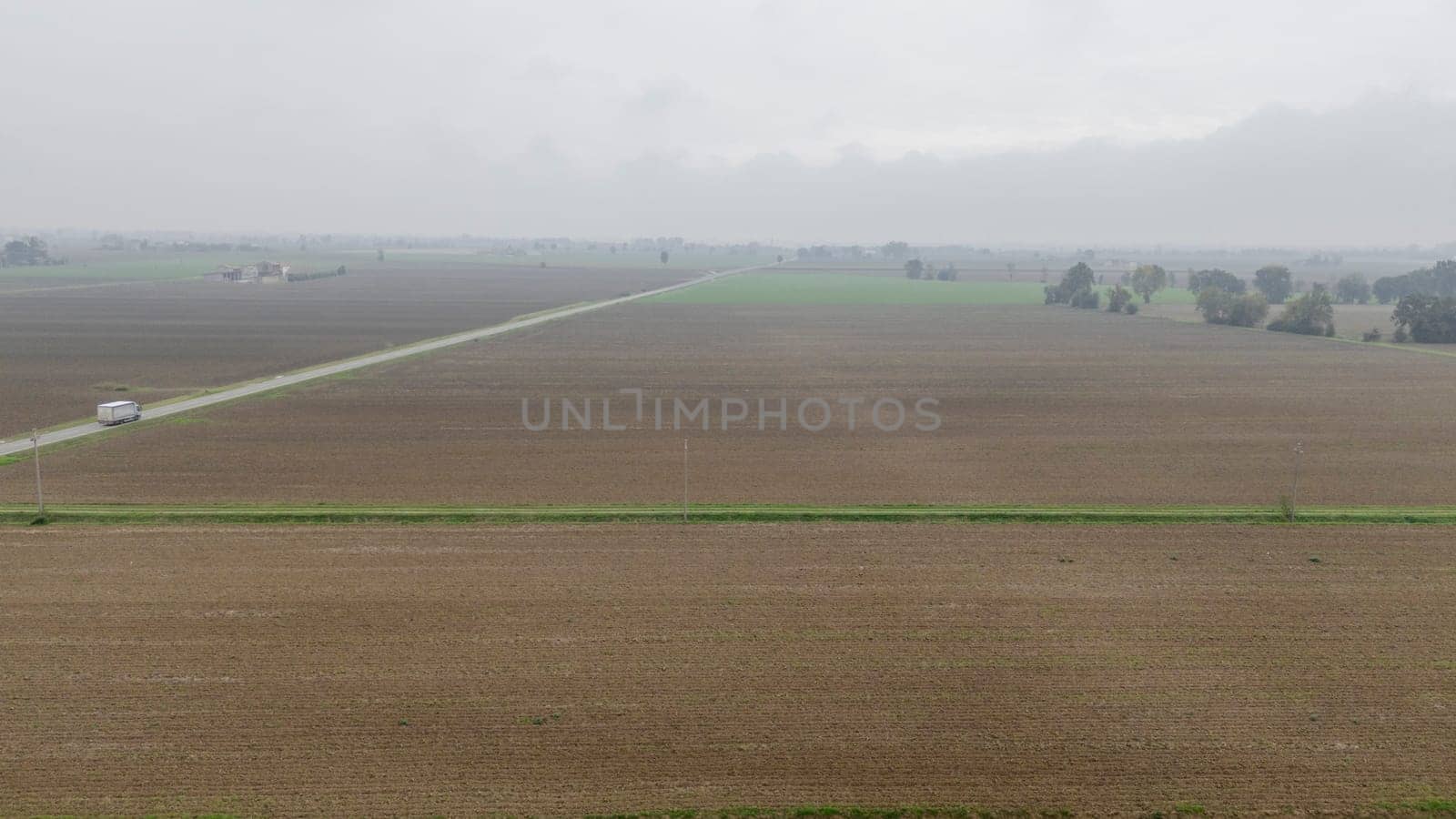 Piacenza, Italy October 15th 2024 A lonely truck is driving on a narrow road crossing the plowed fields of the italian countryside on a cloudy day