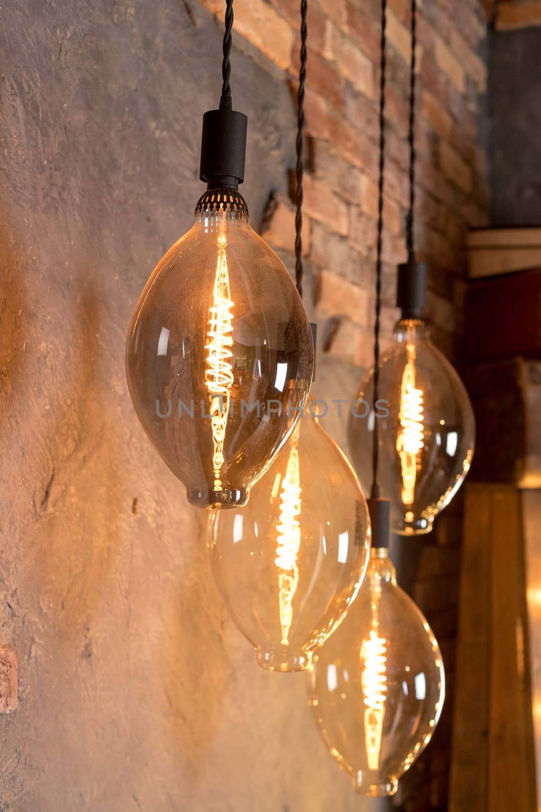 A group of four lighted lamps hanging from the ceiling. The lamps are all different sizes and shapes, but they all have a similar design. The lamps are lit up, creating a warm and inviting atmosphere