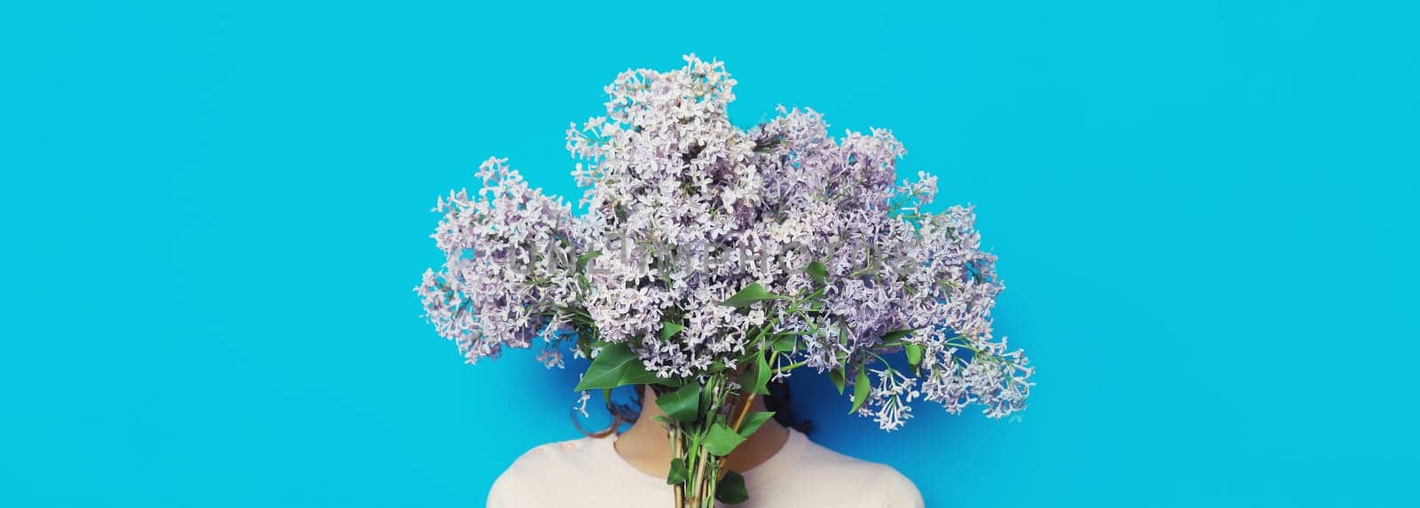Portrait of woman covering her head with bouquet of fresh lilac flowers on blue background