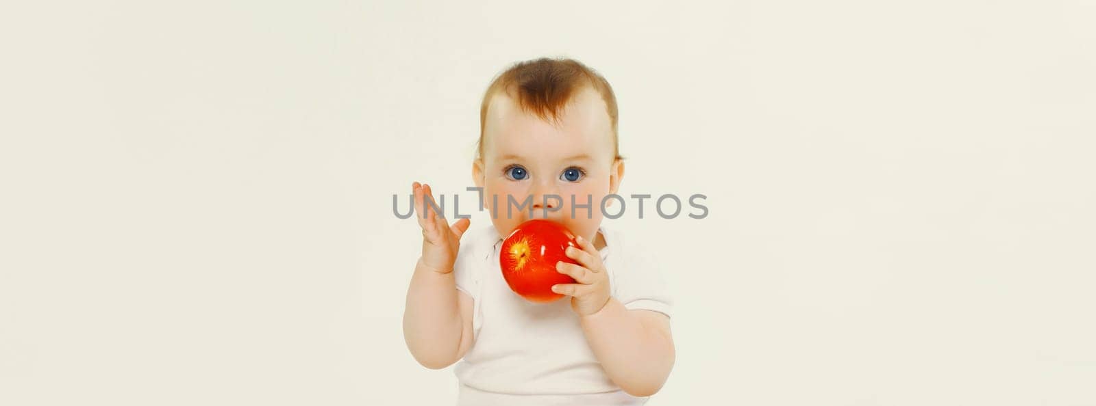 Portrait of cute baby eating red apple fruit sitting isolated on white studio background