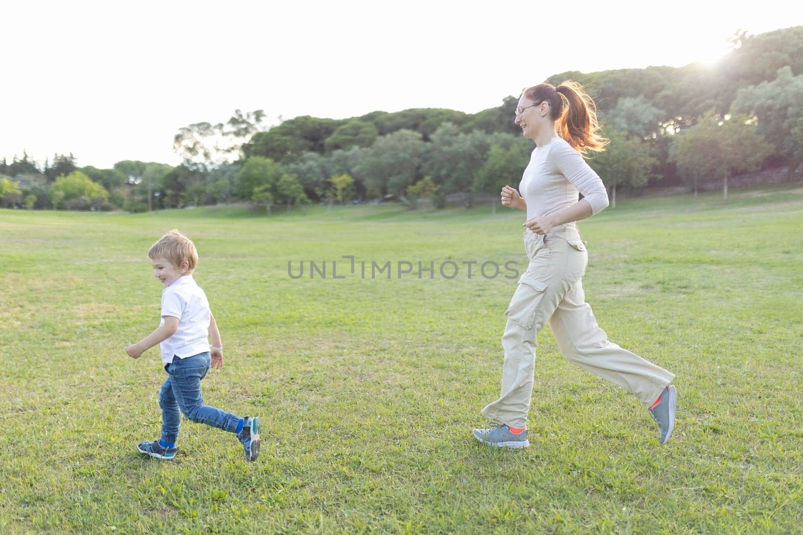 Mother and son are running on the grass in a park, enjoying a beautiful summer day together