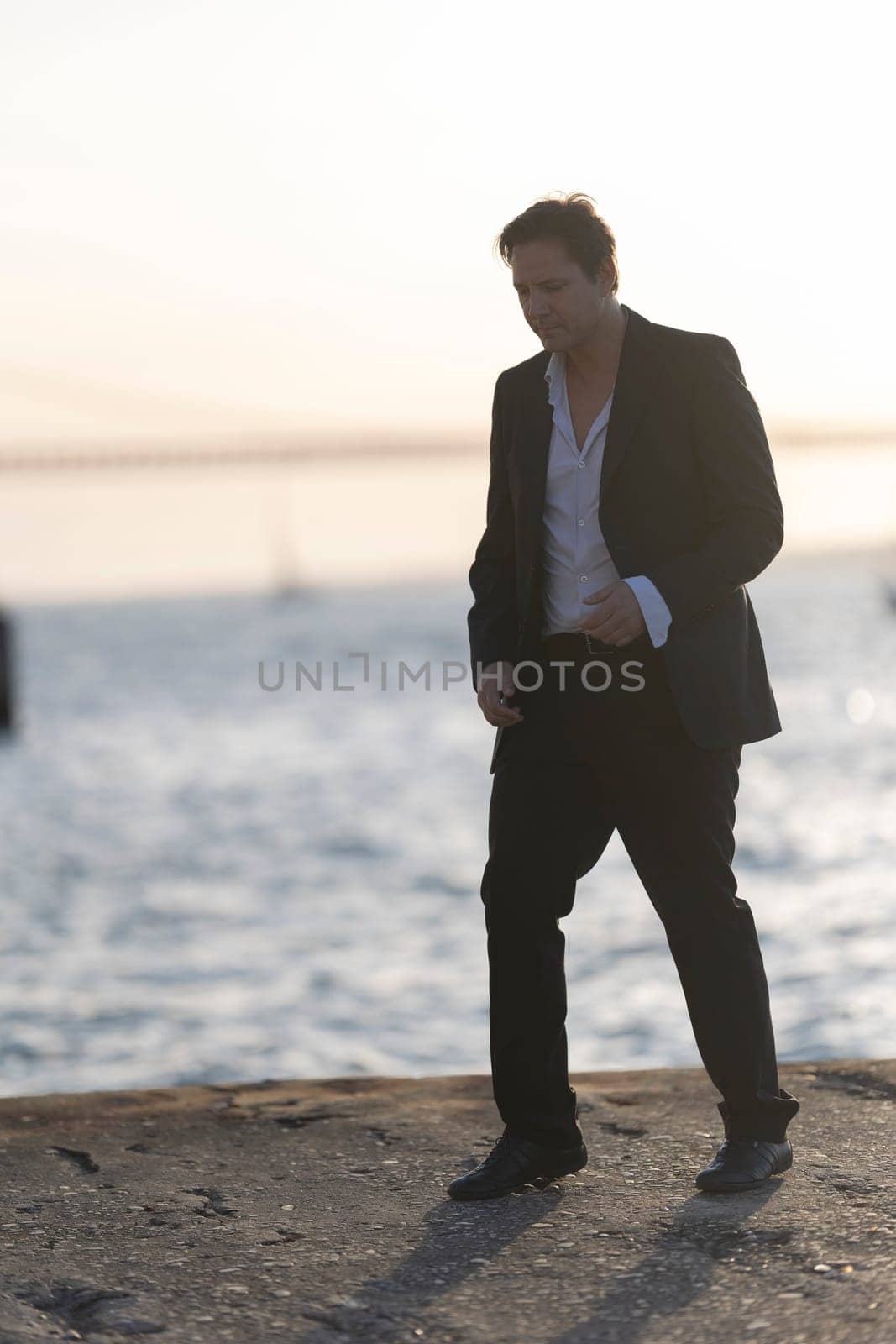 Businessman is walking on a pier at sunset, enjoying the view and the fresh air