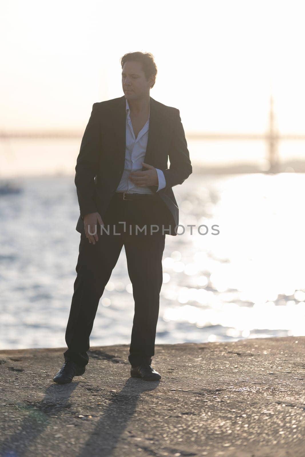 Elegant man is dancing alone by the sea at sunset