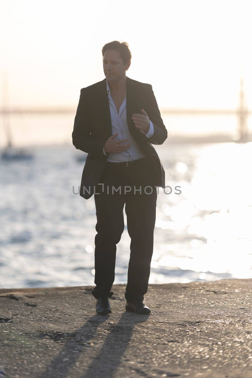 Elegant businessman is dancing by the water at sunset