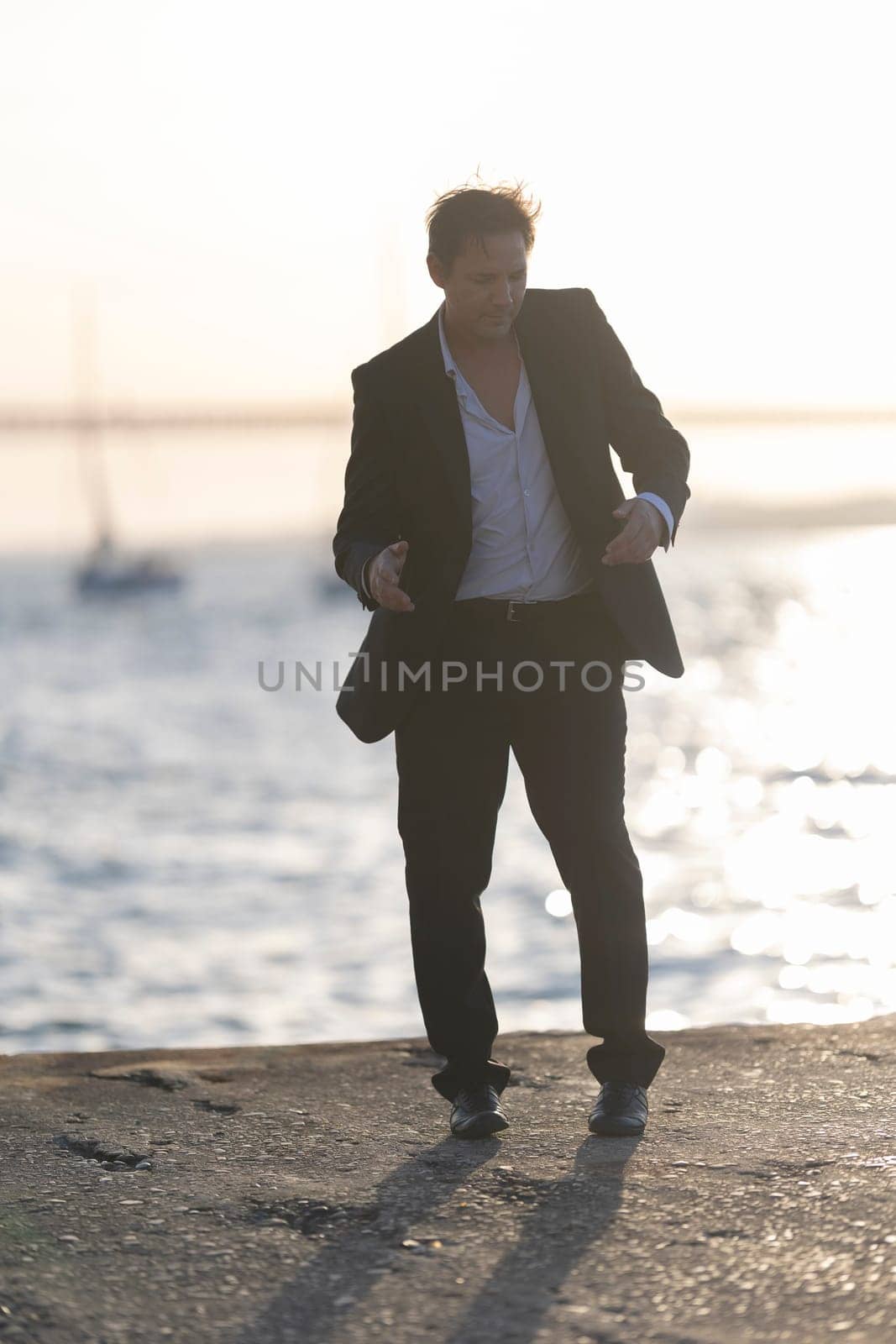 Businessman is happily dancing on a pier by the sea at sunset