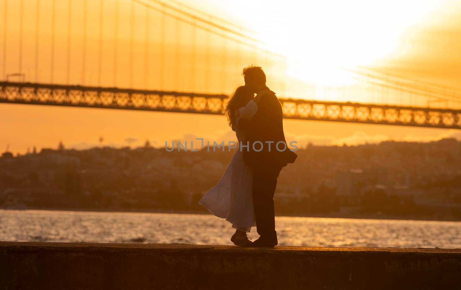 Silhouette of a couple kissing at sunset with a bridge and cityscape in the background
