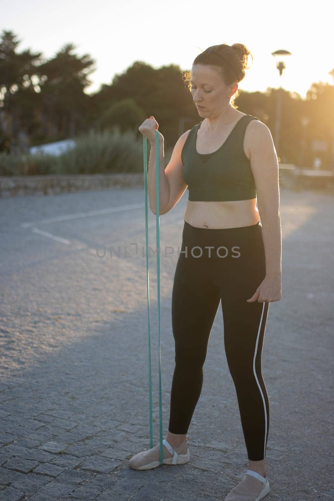 Athletic woman is exercising outdoors, using a resistance band for a biceps curl workout