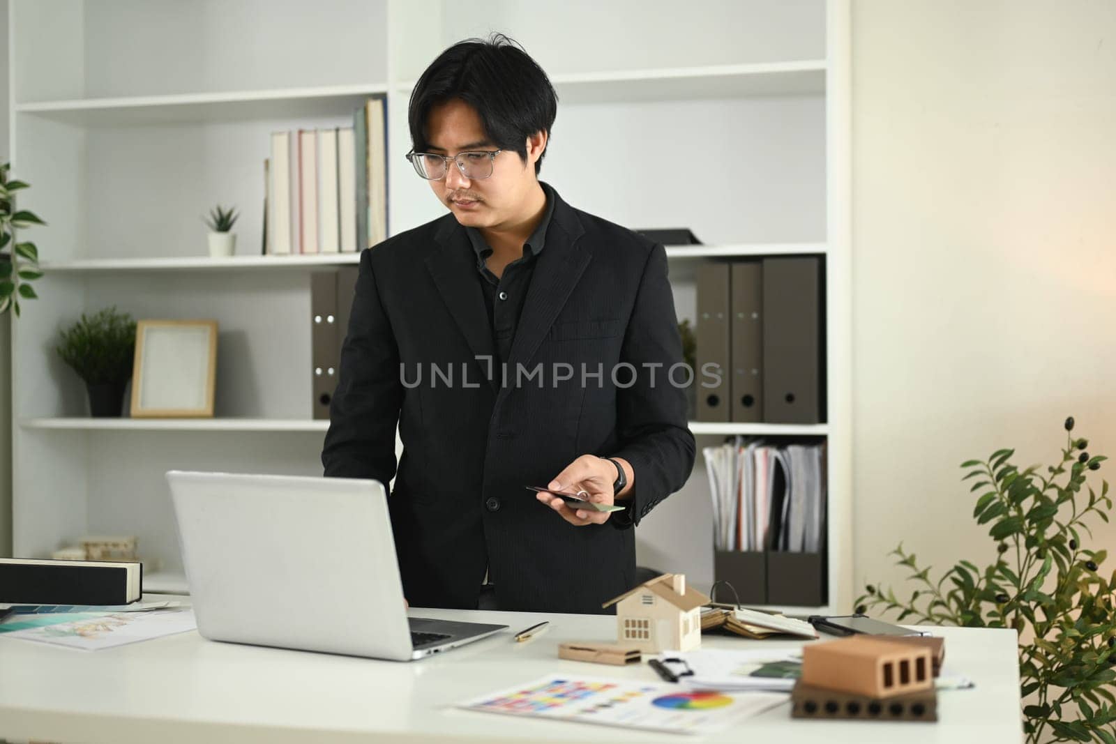Young adult man using laptop, working on a design or architectural project at office.