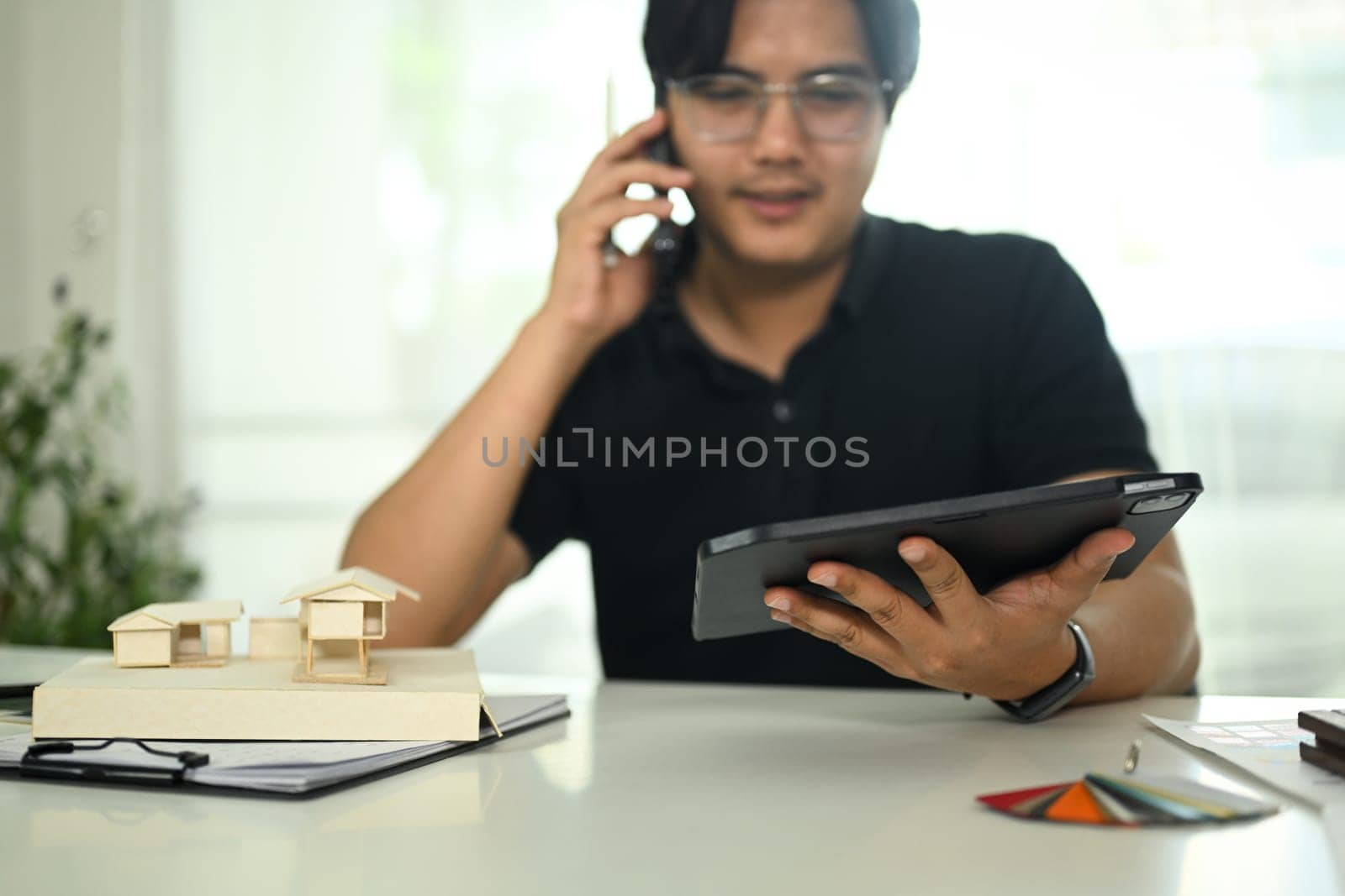 Architect man talking on cell phone and using digital tablet at creative workplace.