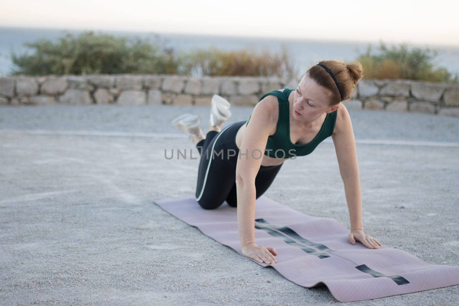 Woman is doing push-ups on a fitness mat near the sea