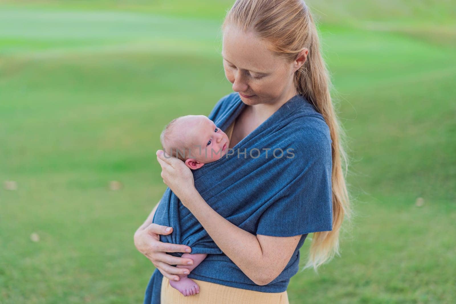 Mom walks with her newborn baby in a sling. This moment highlights the close bond between mother and child, promoting comfort, security, and the benefits of babywearing in everyday life.