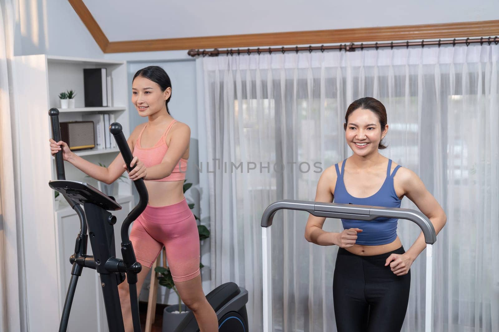 Energetic and strong athletic asian woman running on elliptical running machine at home with workout buddy or trainer. Pursuit of fit physique and commitment to healthy lifestyle. Vigorous