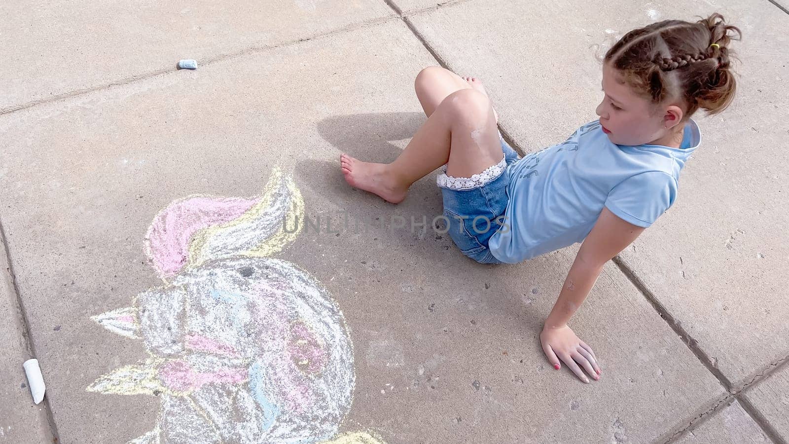 Little girl drawing chalk art on a suburban driveway on a summer day.