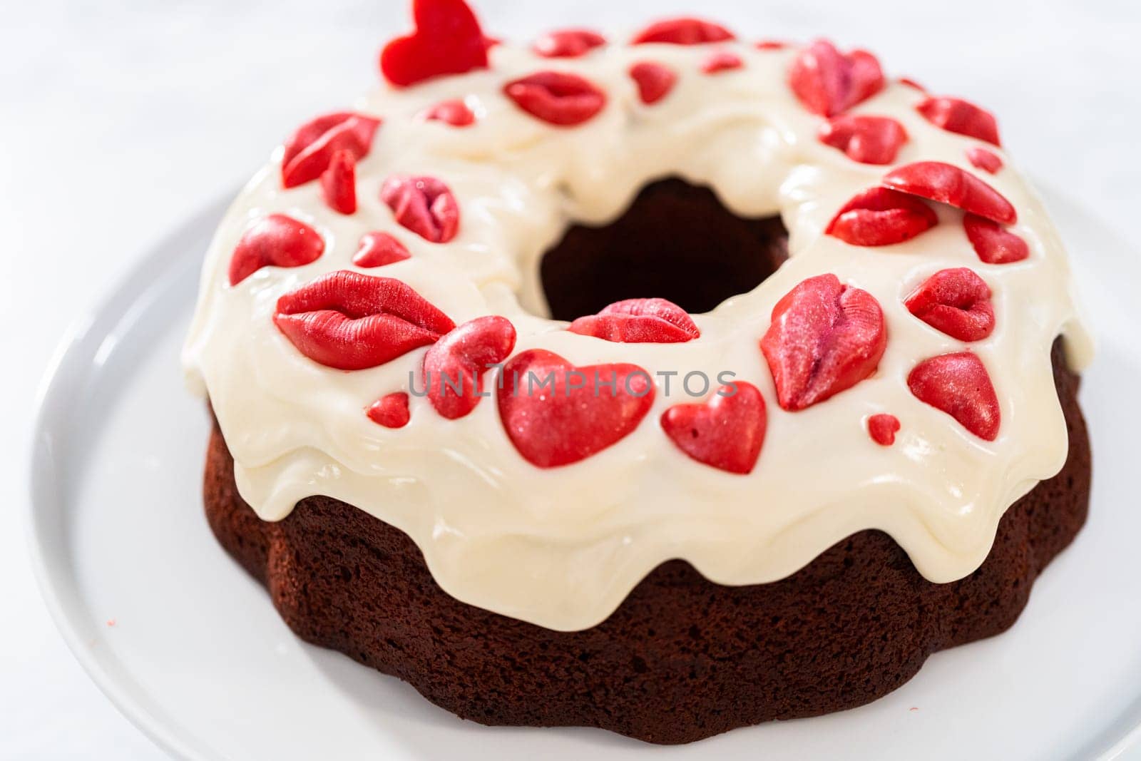 Freshly baked red velvet bundt cake with chocolate lips and hearts over cream cheese glaze for Valentine's Day.