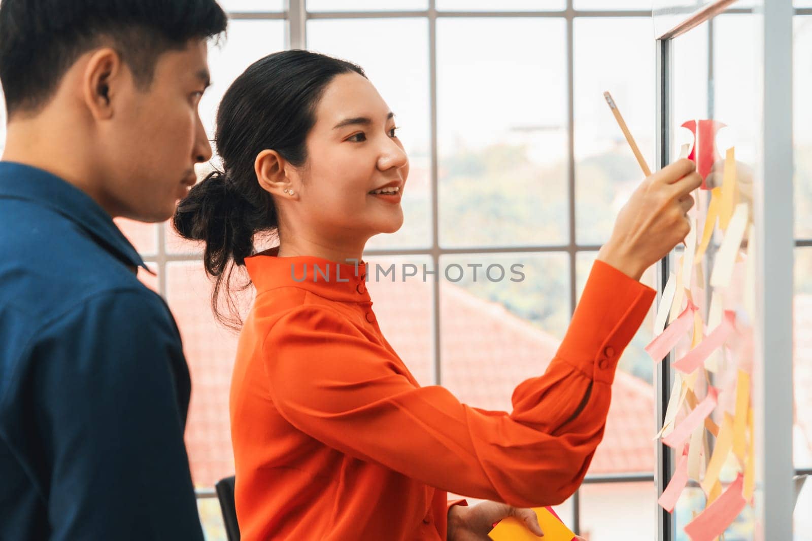 Business people work on project planning board in office and having conversation with coworker friend to analyze project development . They use sticky notes posted on glass to make it organized. Jivy