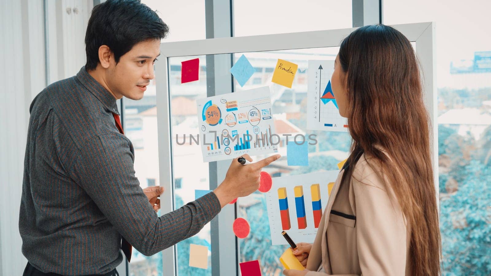 Business people work on project planning board in office and having conversation with coworker friend to analyze project development . They use sticky notes posted on glass to make it organized. Jivy