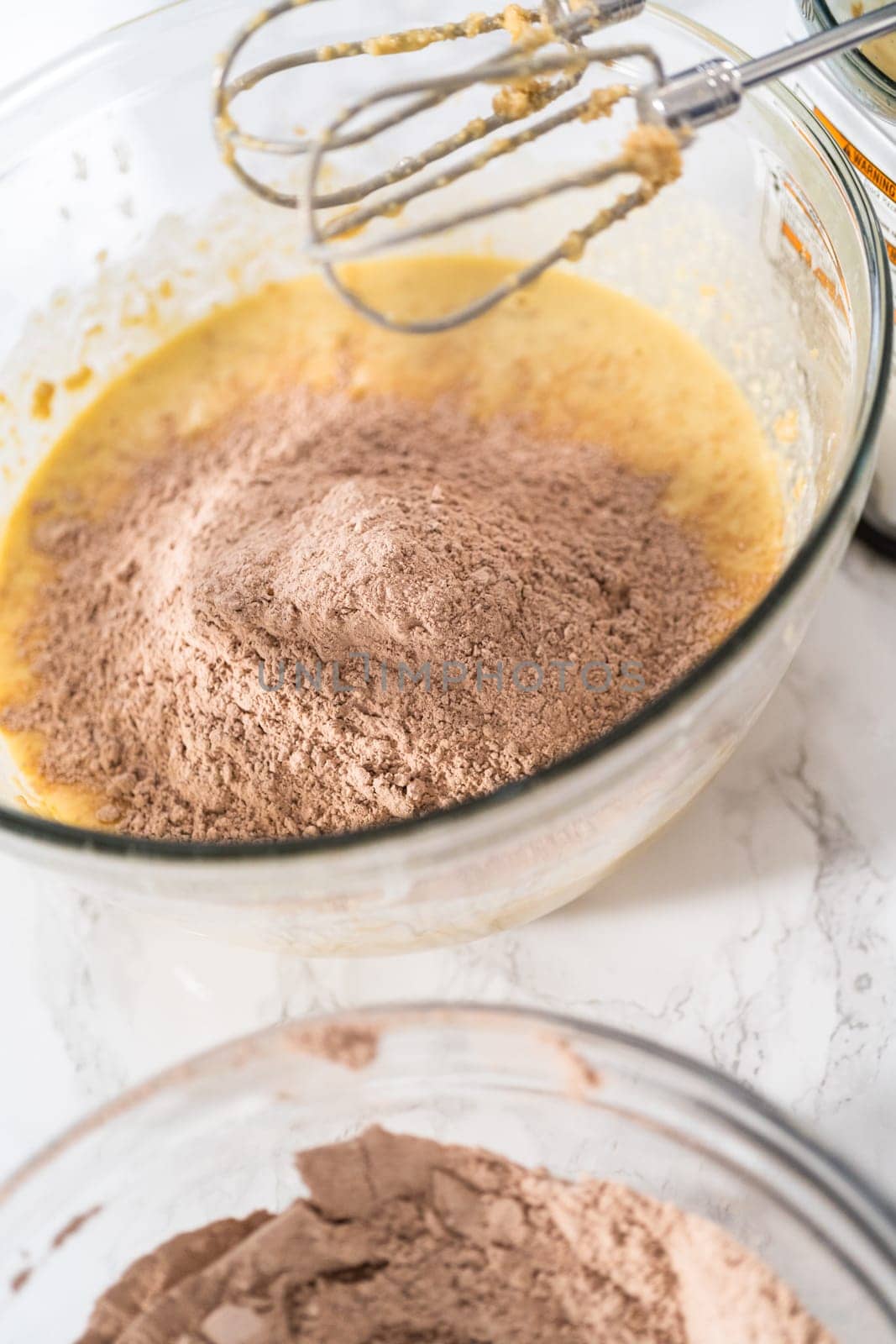 Mixing wet ingredients in a large glass mixing bowl to bake red velvet cupcakes with white chocolate ganache frosting.