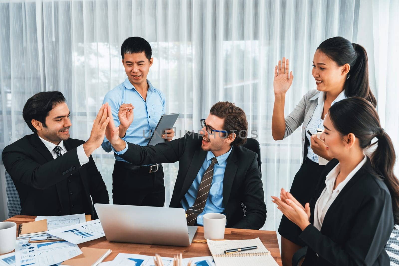 Group of happy businesspeople in high five gesture and successful efficient teamwork. Diverse race office worker celebrate after made progress on marketing planning in corporate office. Meticulous