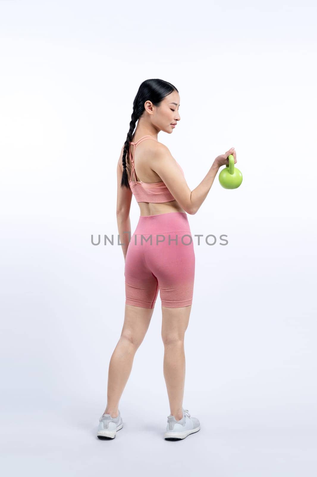 Vigorous energetic woman doing kettlebell weight lifting exercise on isolated background. Young athletic asian woman strength and endurance training session as body workout routine.