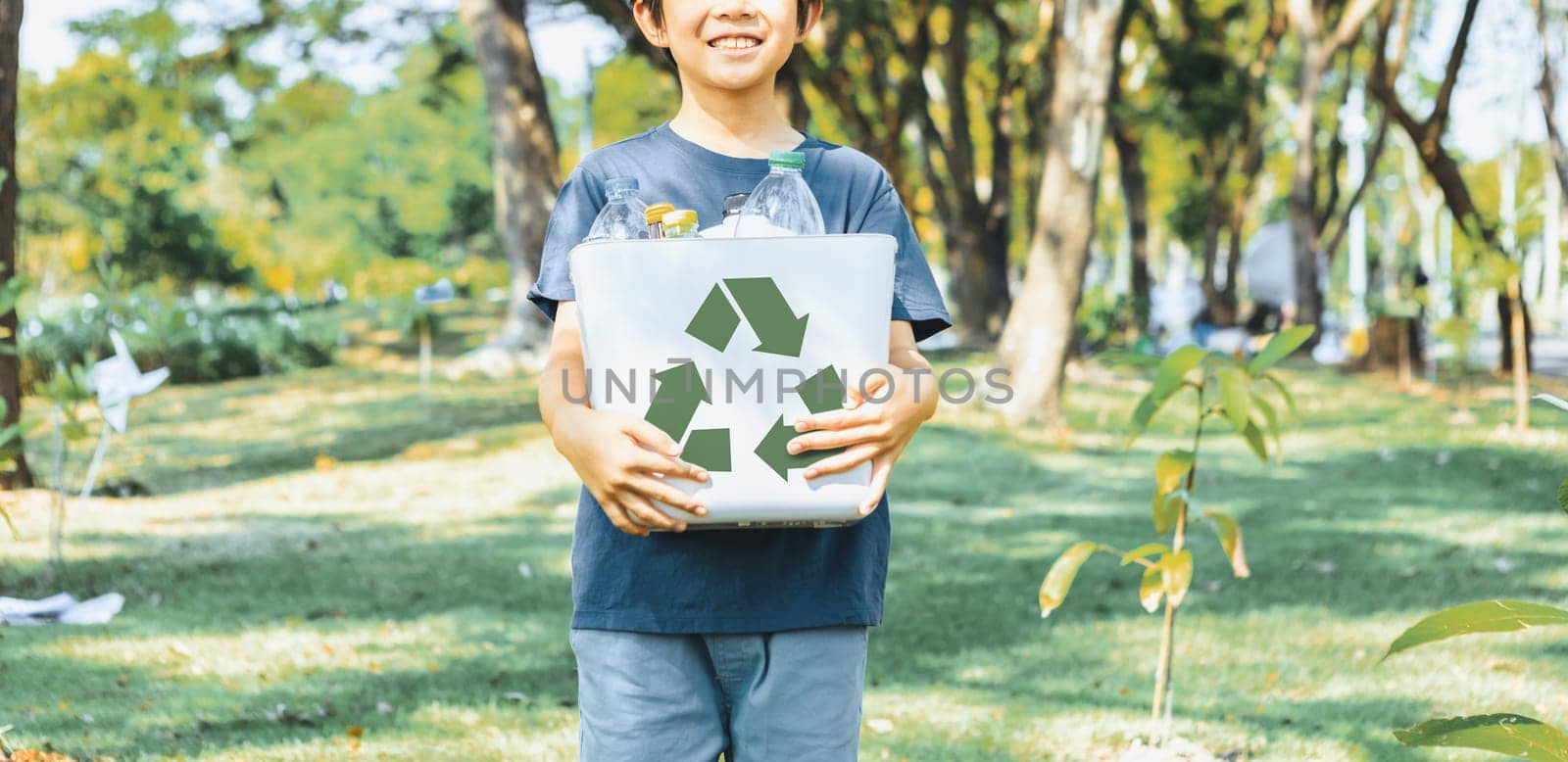 Cheerful young asian boy holding recycle symbol bin on daylight natural green park promoting waste recycle, reduce, and reuse encouragement for eco sustainable awareness for future generation. Gyre