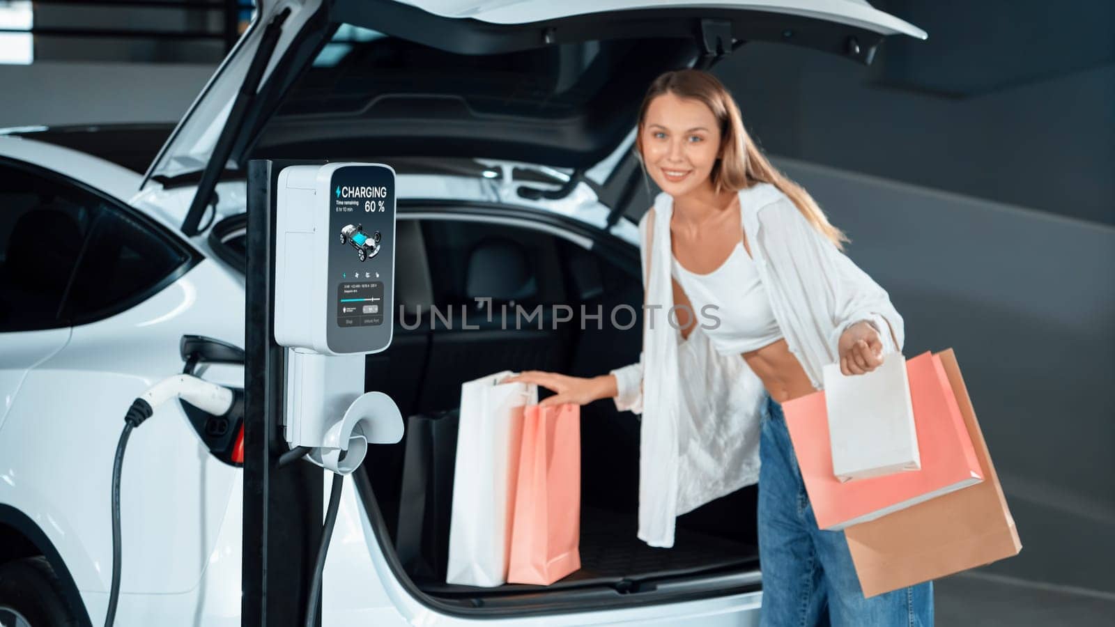 Young woman travel with EV electric car to shopping center parking lot charging in downtown city showing urban sustainability lifestyle by green clean rechargeable energy of electric vehicle innards