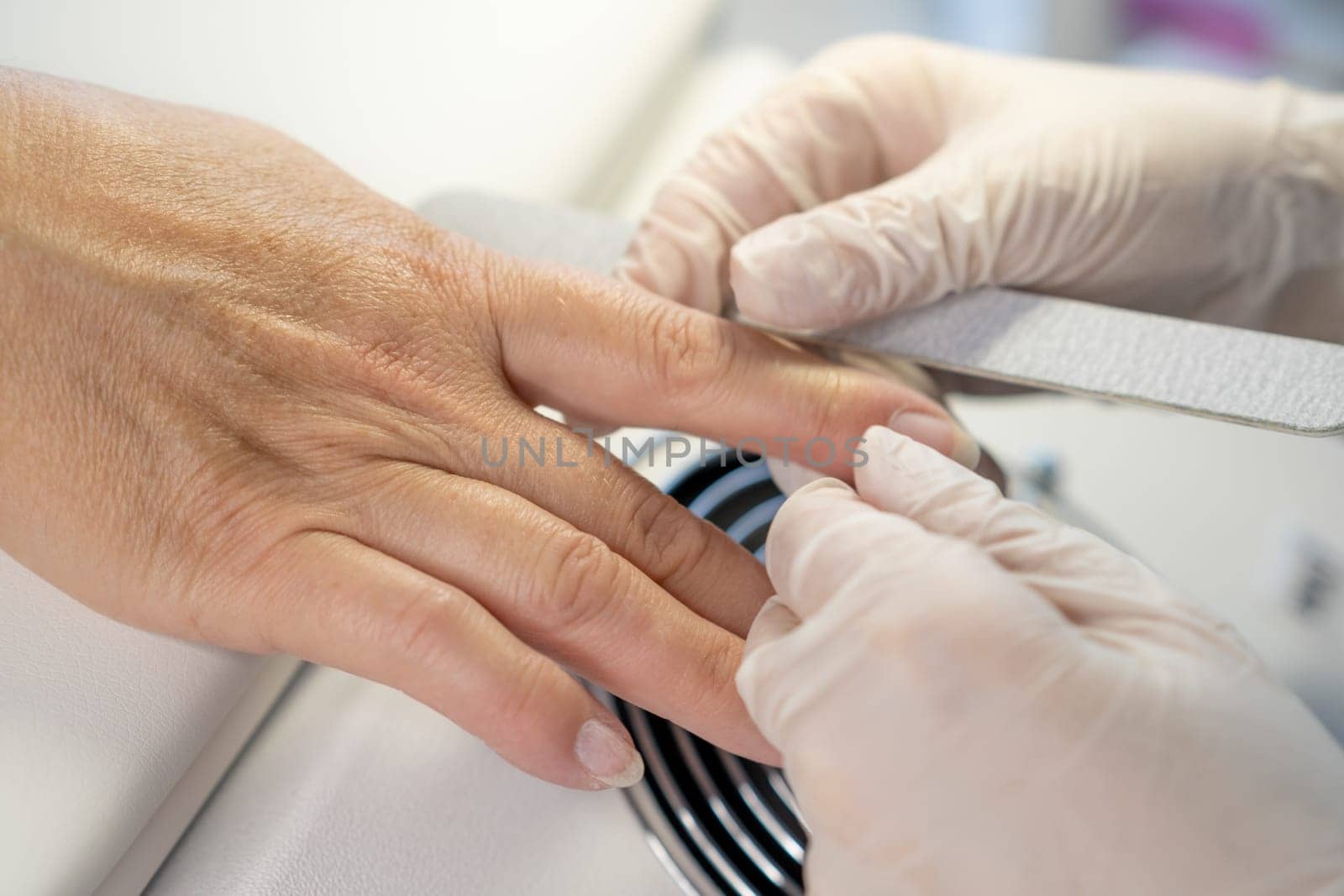 Nail care procedure in a beauty salon. Female hands and tools for manicure, process of performing manicure in beauty salon. Gloved hands of a skilled manicurist cutting cuticles. Concept spa body care