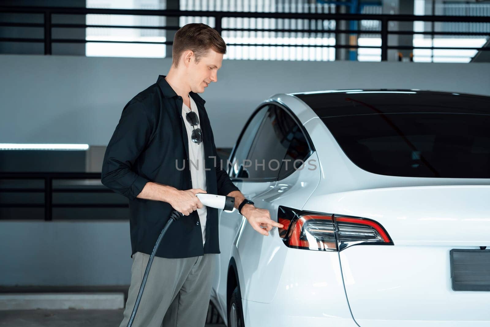 Young man travel with EV electric car to shopping center parking lot charging in downtown city showing urban sustainability lifestyle by green clean rechargeable energy of electric vehicle innards