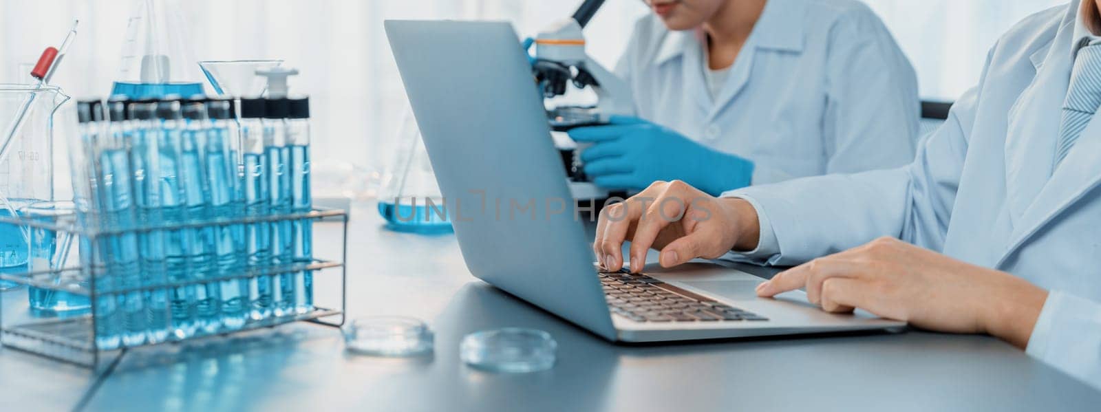 Dedicated group of scientist conduct chemical experiments and research in medical lab as groundbreaking developing for new vaccine drug or antibiotic and studying test result on laptop. Neoteric