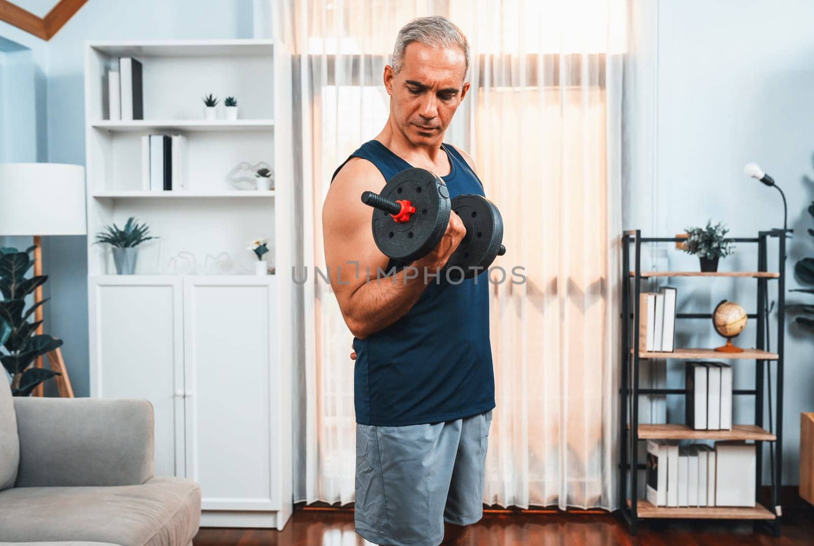 Athletic and sporty senior man lifting dumbbell at home. Clout by biancoblue
