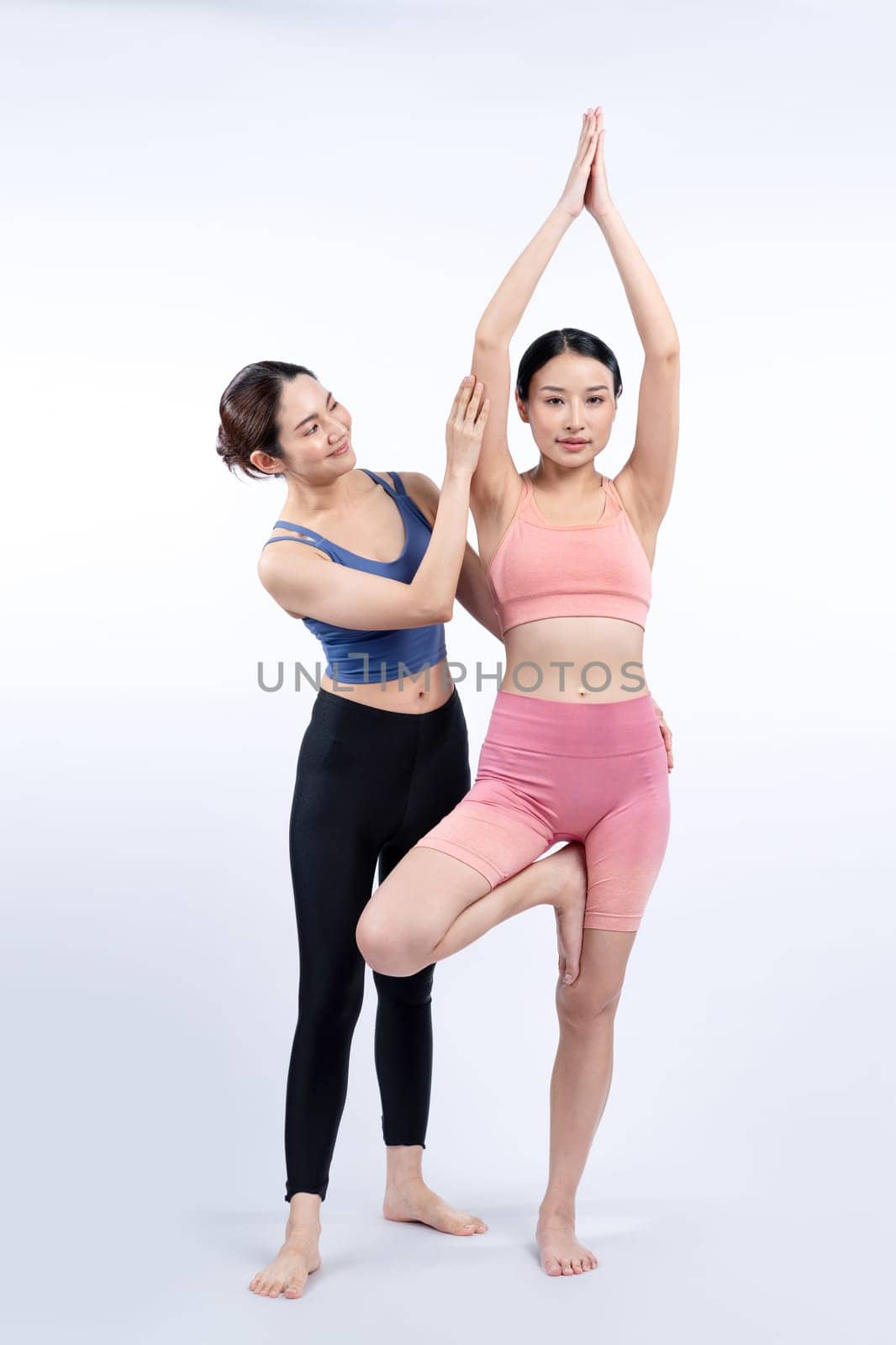 Asian woman in sportswear doing yoga exercise in standing pose with her trainer or yoga buddy. Healthy body care and meditation yoga lifestyle in full shot on isolated background. Vigorous