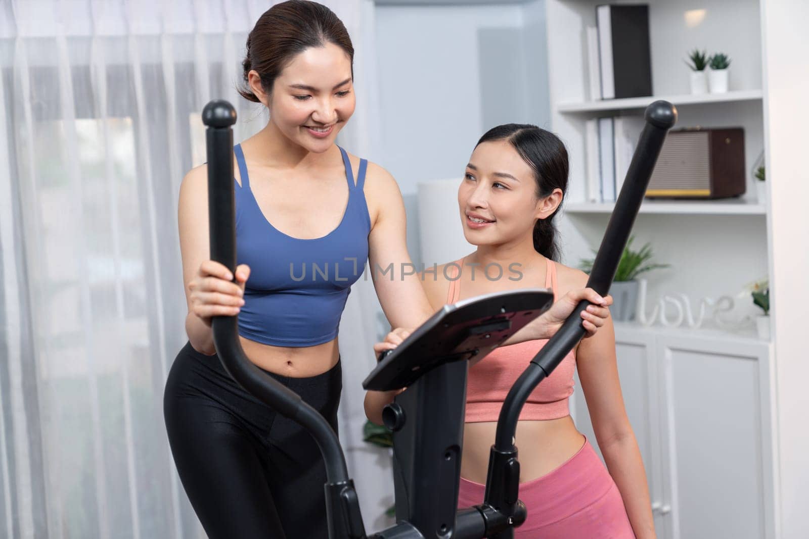 Energetic and strong athletic asian woman running on elliptical running machine at home with workout buddy or trainer. Pursuit of fit physique and commitment to healthy lifestyle. Vigorous