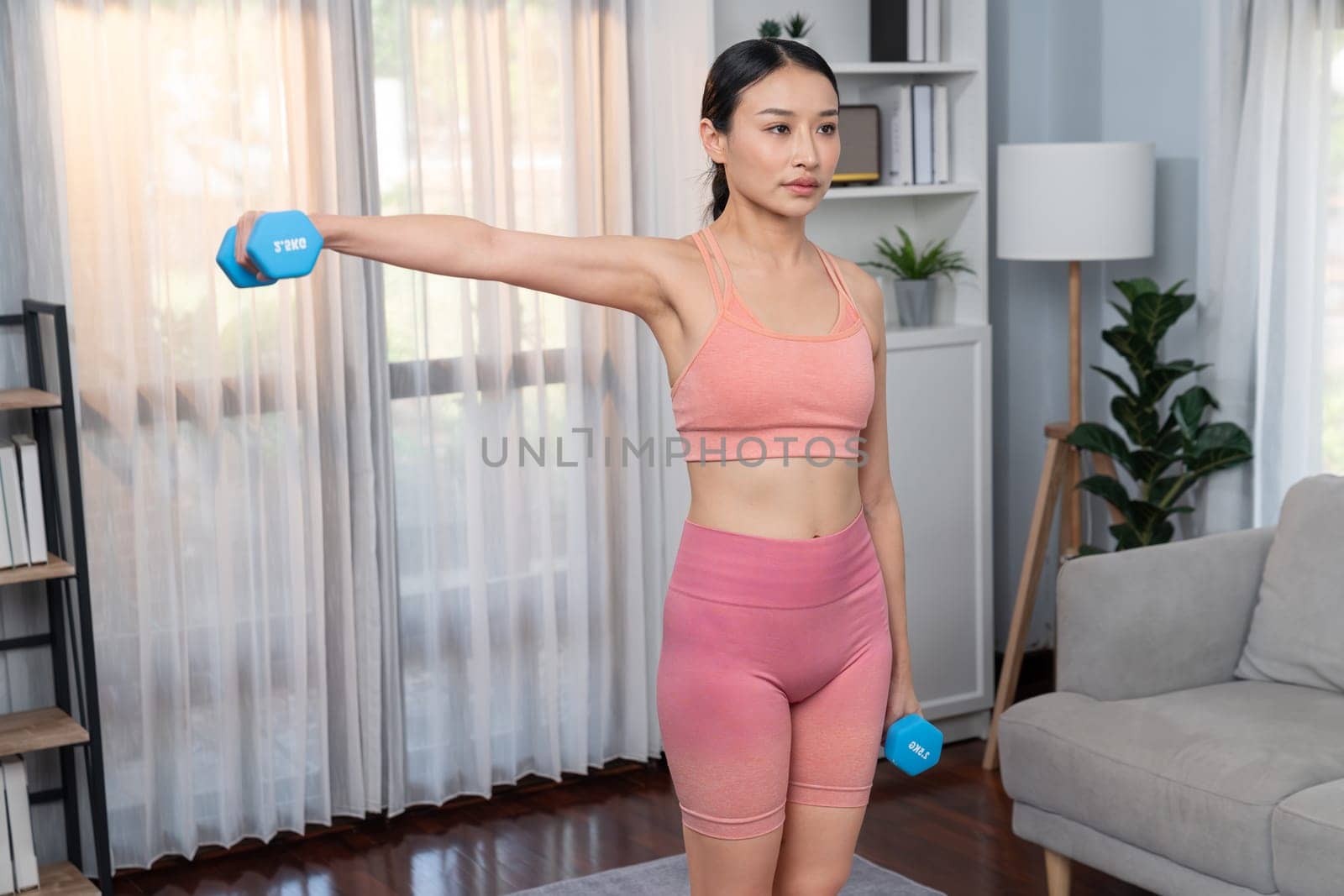 Vigorous energetic woman doing yoga with dumbbell weight lifting exercise at home. Young athletic asian woman strength and endurance training session as home workout routine.