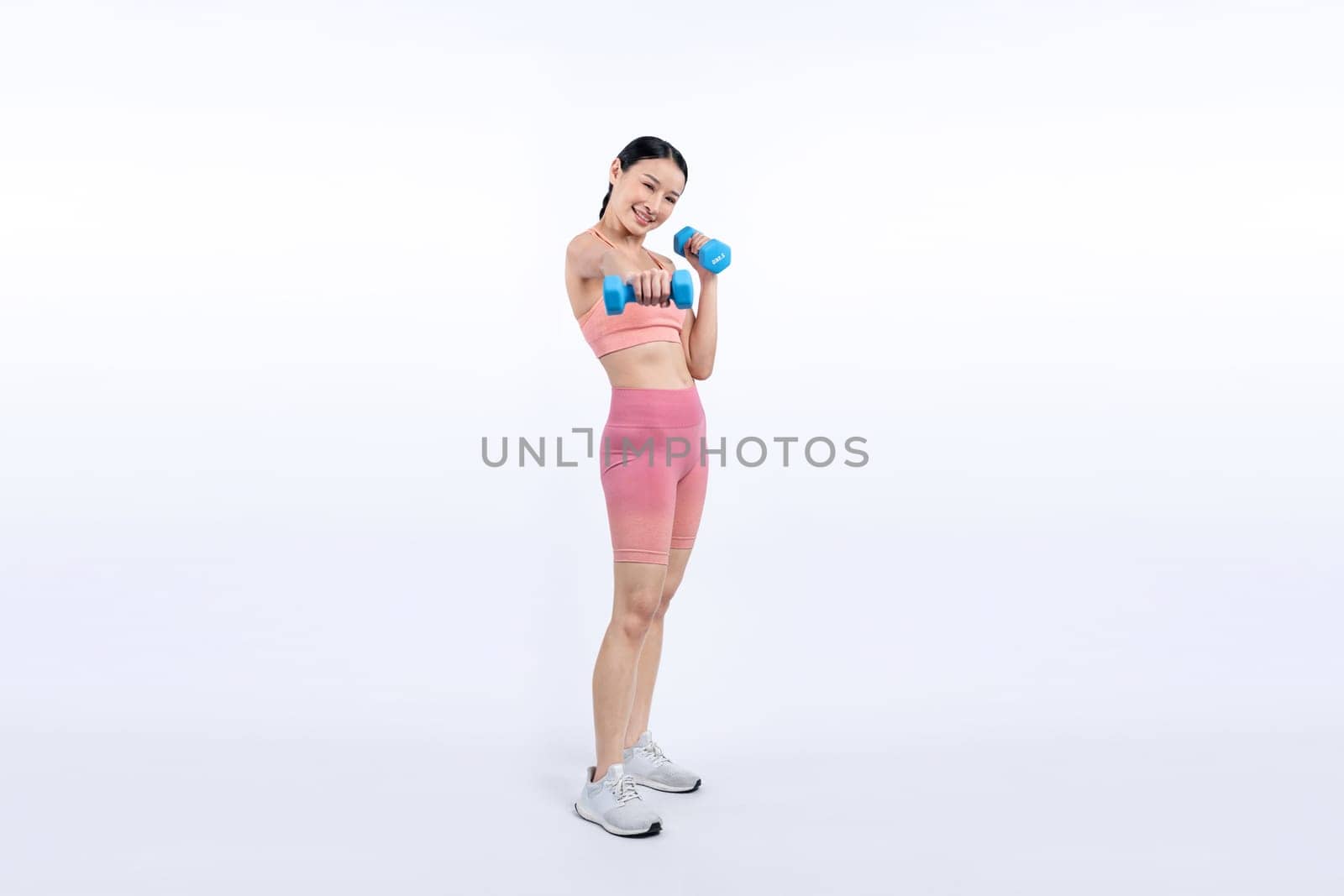 Vigorous energetic woman doing dumbbell weight lifting exercise on isolated background. Young athletic asian woman strength and endurance training session as body workout routine.