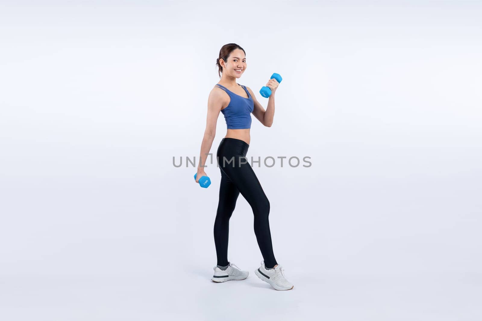 Vigorous energetic woman doing dumbbell weight lifting exercise on isolated background. Young athletic asian woman strength and endurance training session as body workout routine.