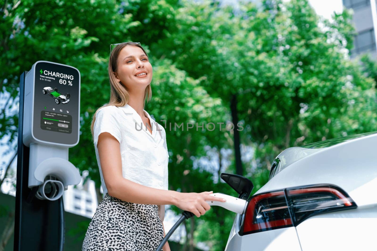 Young woman travel with EV electric car charging in green sustainable city outdoor garden in summer. Urban sustainability lifestyle by green clean rechargeable energy of electric BEV vehicle innards