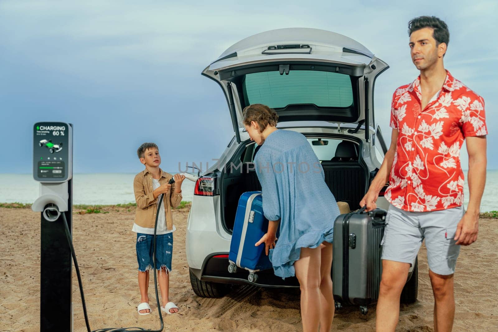 Family vacation trip traveling by the beach with electric car, lovely family taking luggage out while charging EV car battery with clean energy. Alternative family travel by eco-friendly car.Perpetual
