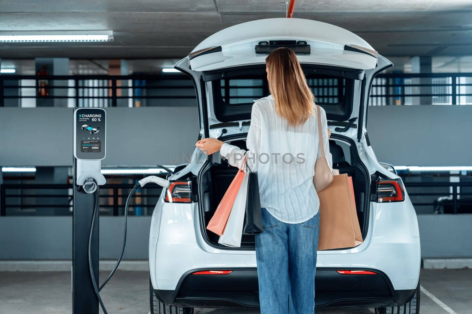 Young woman travel with EV electric car to shopping center parking lot charging in downtown city showing urban sustainability lifestyle by green clean rechargeable energy of electric vehicle innards