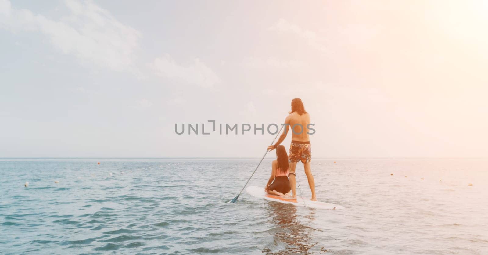 Sea woman and man on sup. Silhouette of happy young woman and man, surfing on SUP board, confident paddling through water surface. Idyllic sunset. Active lifestyle at sea or river