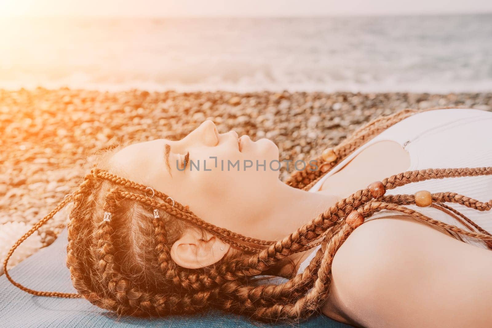 Woman sea yoga. Well looking middle aged woman with braids dreadlocks in white leggings and tops doing stretching pilates on yoga mat near sea. Female fitness yoga routine concept. Healthy lifestyle. by panophotograph