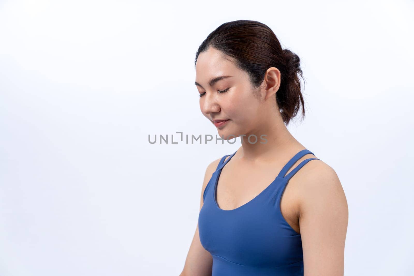 Asian woman in sportswear doing yoga exercise on fitness mat as her workout training routine. Healthy body care and calm meditation in yoga lifestyle in full body shot on isolated background. Vigorous