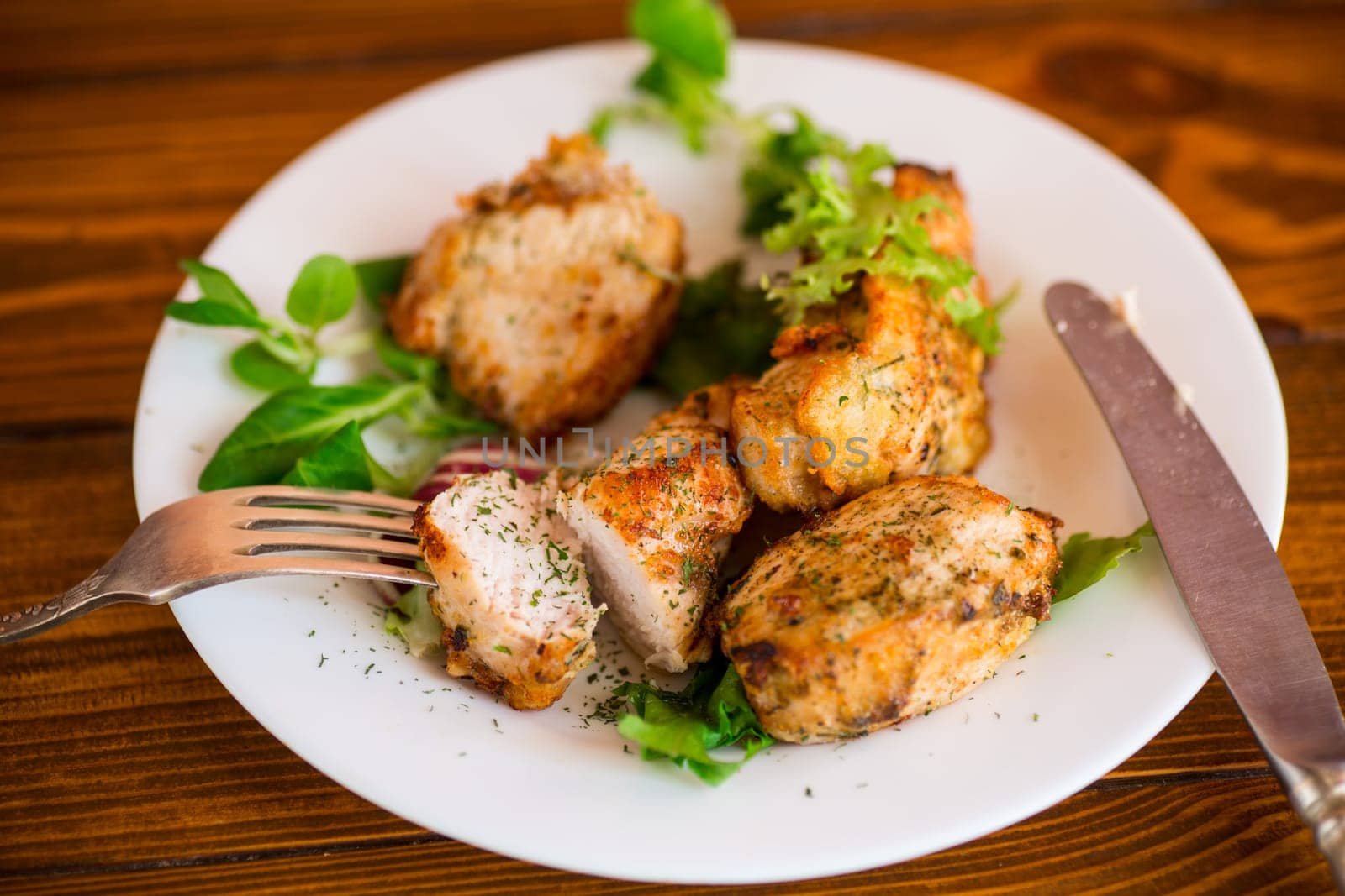 Fried pieces of chicken fillet breaded with spices and herbs in a plate on a wooden table.