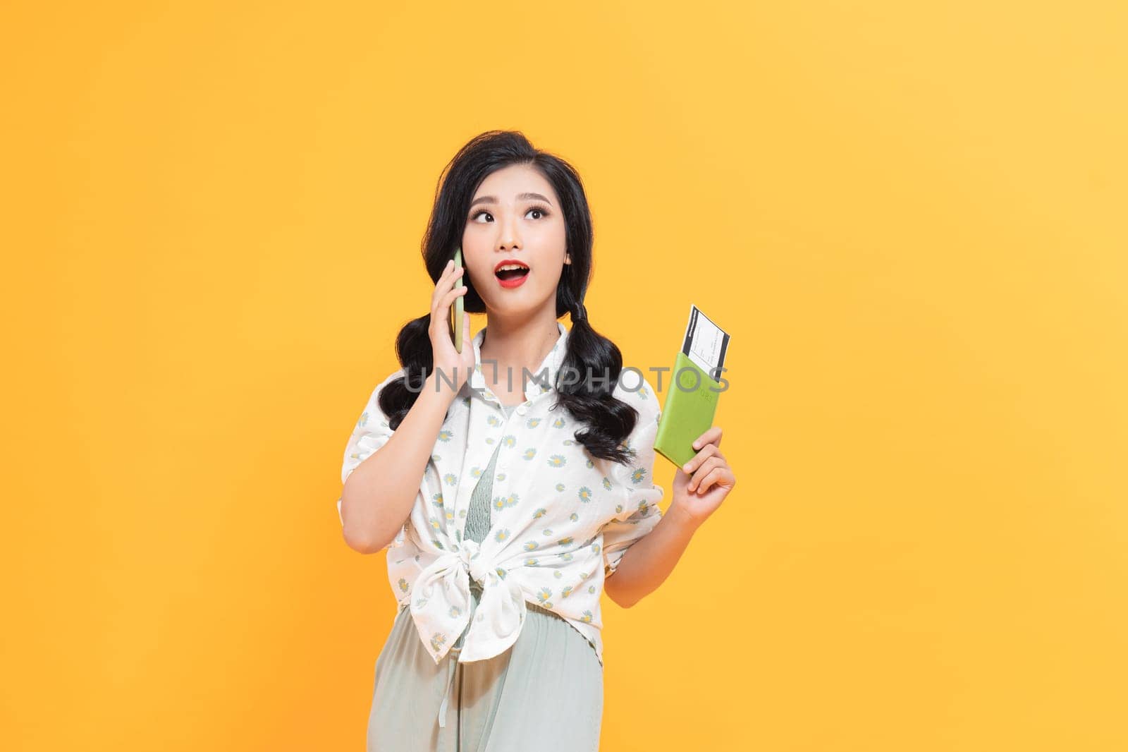 Smiling woman holding passport with tickets and talking on cellphone isolated over yellow background by makidotvn