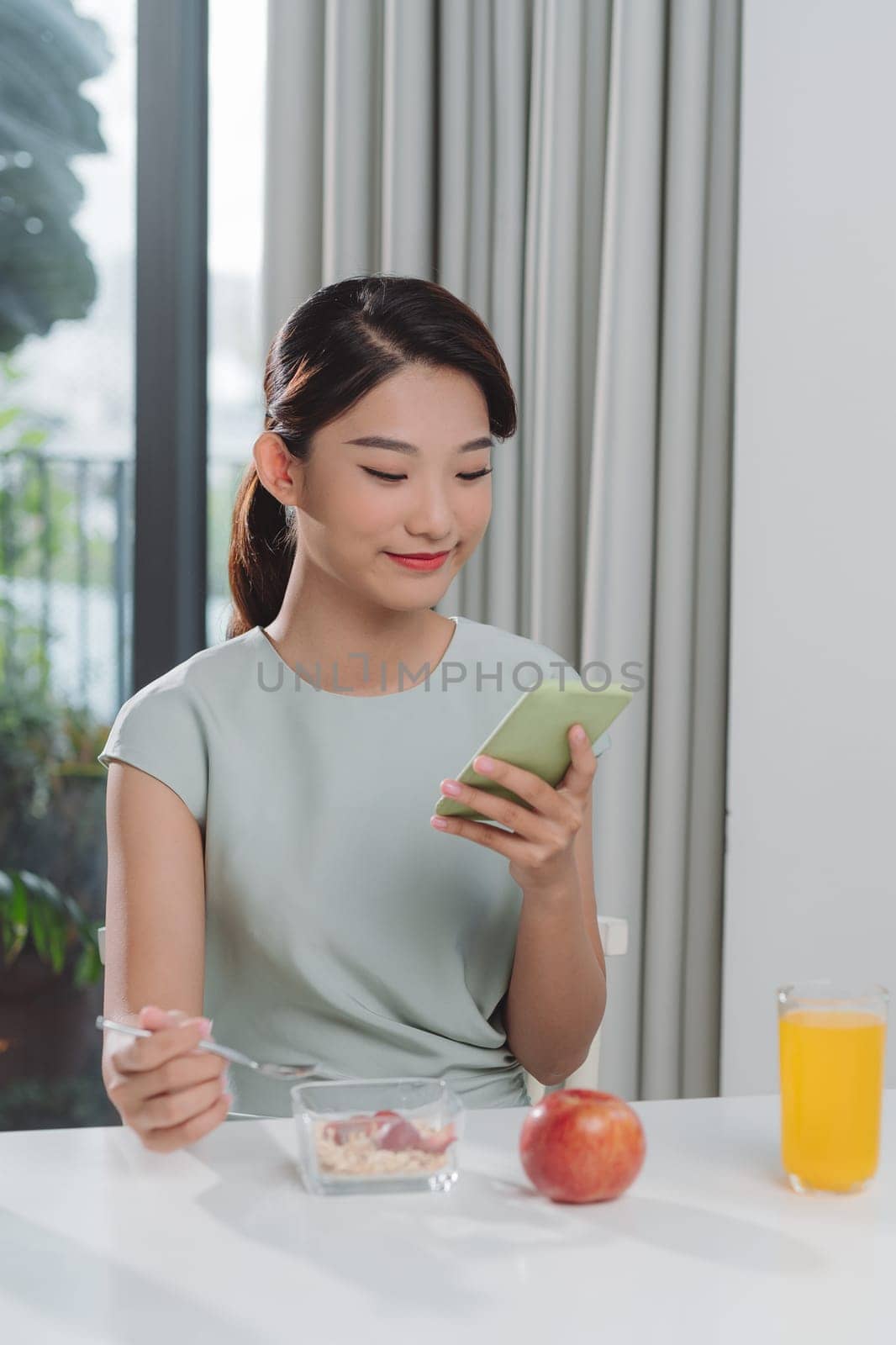 Woman is looking for information on Internet, using mobile, during eating breakfast. 