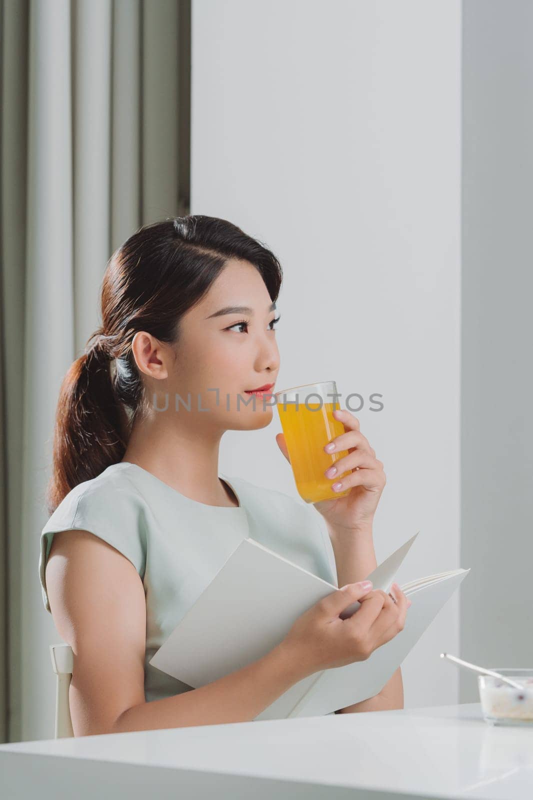 Asian woman reading a book and hold orange juice glass in the home by makidotvn